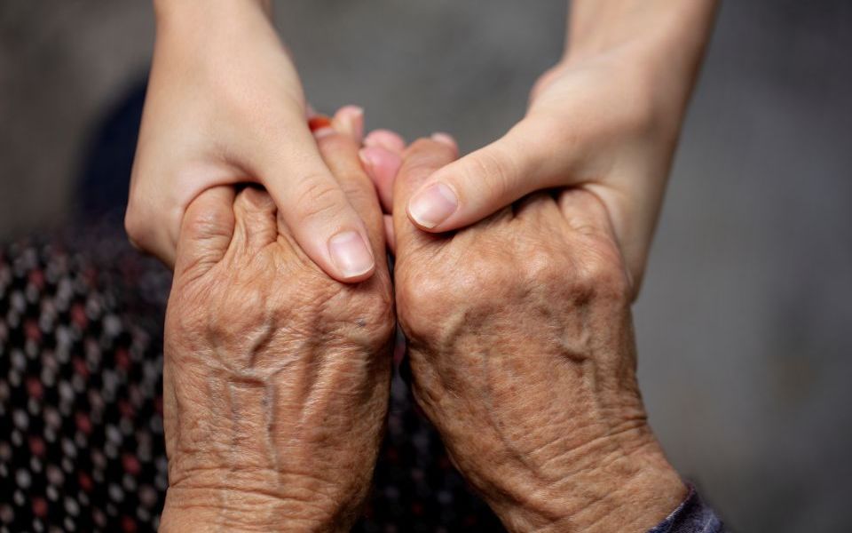 handen van een ouder persoon en een jonger persoon die elkaar vasthouden